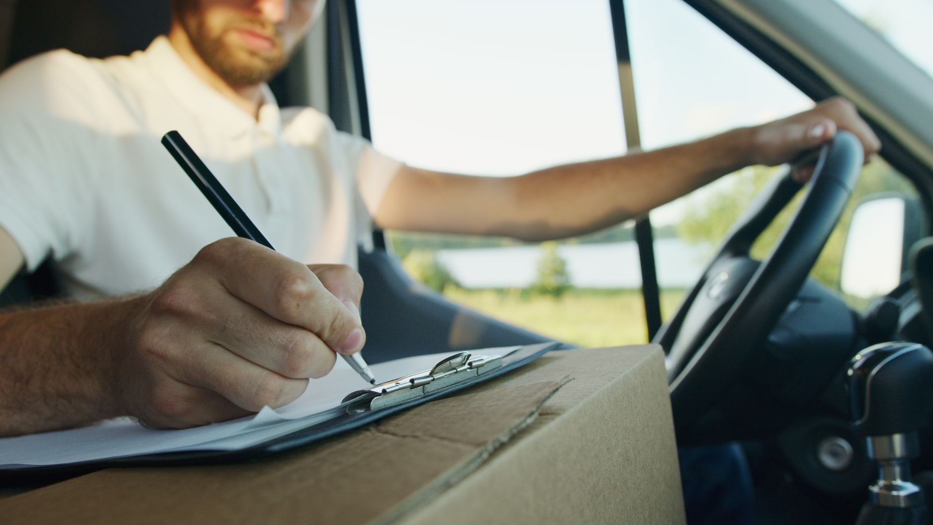 Close-up of a delivery driver inside a van writing on a clipboard